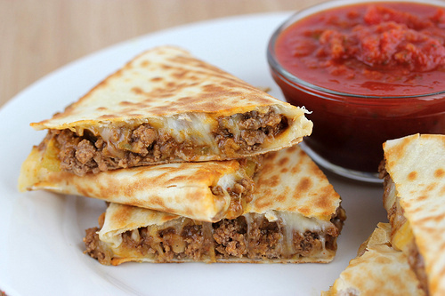 Beef quesadilla slices served with salsa in a white plate