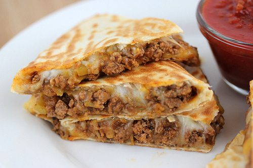 Beef quesadilla slices served with salsa in a white plate