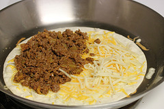 Tortilla in pan topped with melted cheese and seasoned ground beef