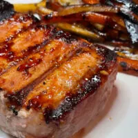 Honey garlic grilled pork chop on white plate with roasted carrots and parsnips.