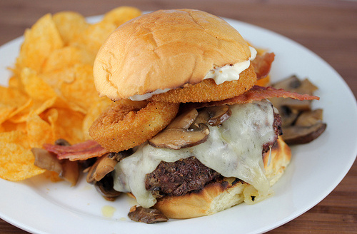 Steakhouse burger with beef patty, cheese, bacon, onion rings, mushrooms, and chips on the side