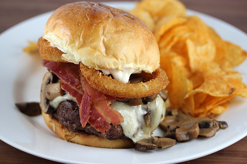 Steakhouse burger with beef patty, cheese, bacon, onion rings, mushrooms, and chips on the side