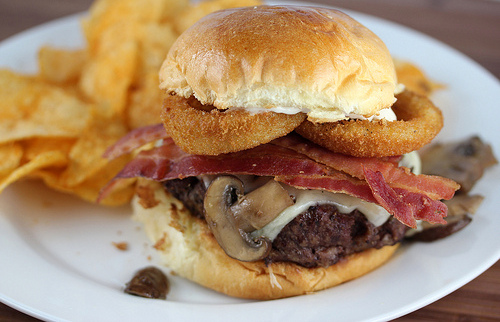 Steakhouse burger with beef patty, cheese, bacon, onion rings, mushrooms, and chips on the side