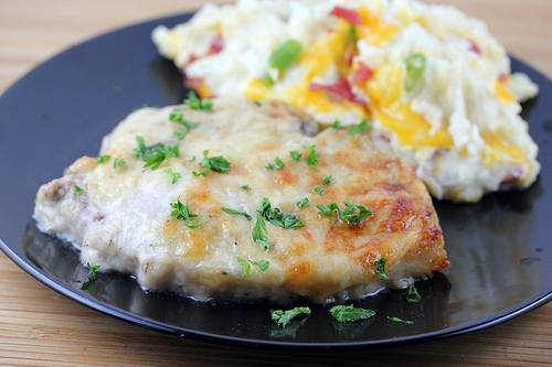 Baked Caesar pork chop garnished with parsley served with cheesy mashed potatoes