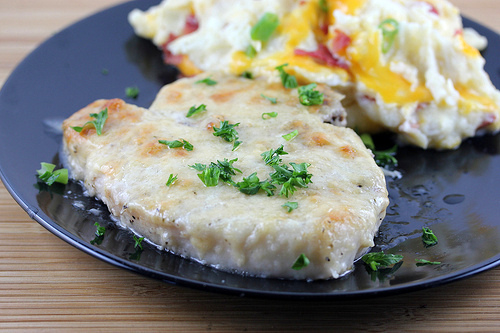Baked Caesar pork chop garnished with parsley served with cheesy mashed potatoes