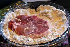 Raw pork chop dredged in seasoned flour mixture in a glass dish