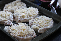 Raw pork chops coated in Caesar dressing and shredded cheese on a baking sheet