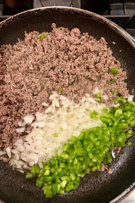 Ground beef, onions, and peppers in a saucepan