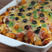 Baked taco tater tot casserole topped with melted cheese and black olives in a white dish