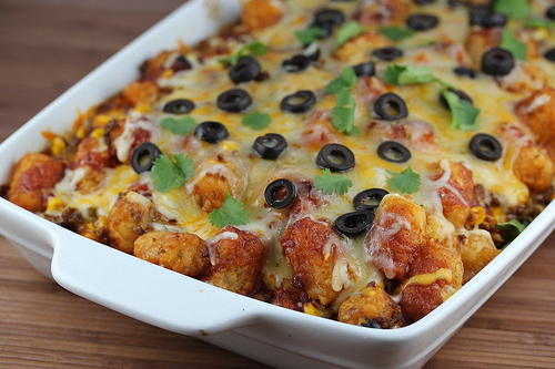 Baked taco tater tot casserole topped with melted cheese and black olives in a white dish