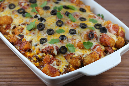 Baked taco tater tot casserole topped with melted cheese and black olives in a white dish