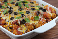 Baked taco tater tot casserole topped with melted cheese and black olives in a white dish