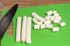 Sliced mozzarella sticks on a green cutting board with knife