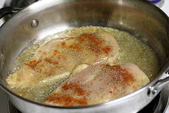 Chicken breast cooking in a skillet with sauce