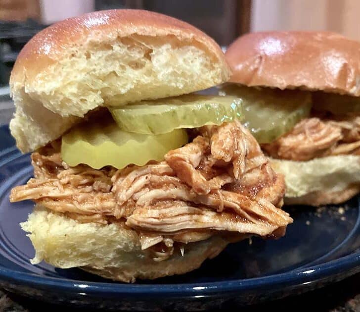 Slow cooker pulled chicken prepared in slider buns with pickles.