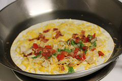 Chicken quesadilla cooking in a skillet with cheese, bacon, and pico de gallo