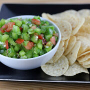 Bowl of green pepper salsa with tortilla chips on a black plate