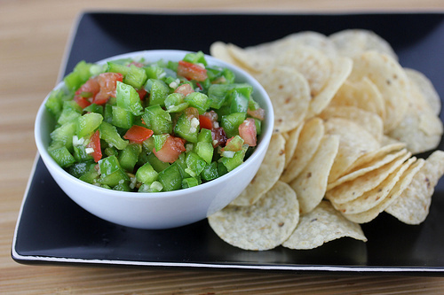 Bowl of green pepper salsa with tortilla chips on a black plate