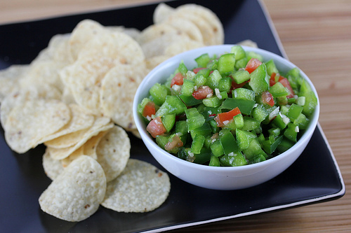 Bowl of green pepper salsa with tortilla chips on a black plate