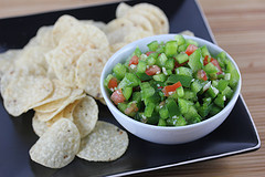 Bowl of green pepper salsa with tortilla chips on a black plate