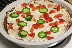 Close‑up of bubbling baked taco dip with seasoned ground beef, beans, sour cream layer, and melted cheese