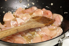 Raw chicken pieces cooking in a pan with wooden spatula