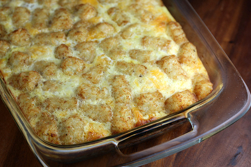 Baked tater tot breakfast casserole topped with melted cheese in a glass dish
