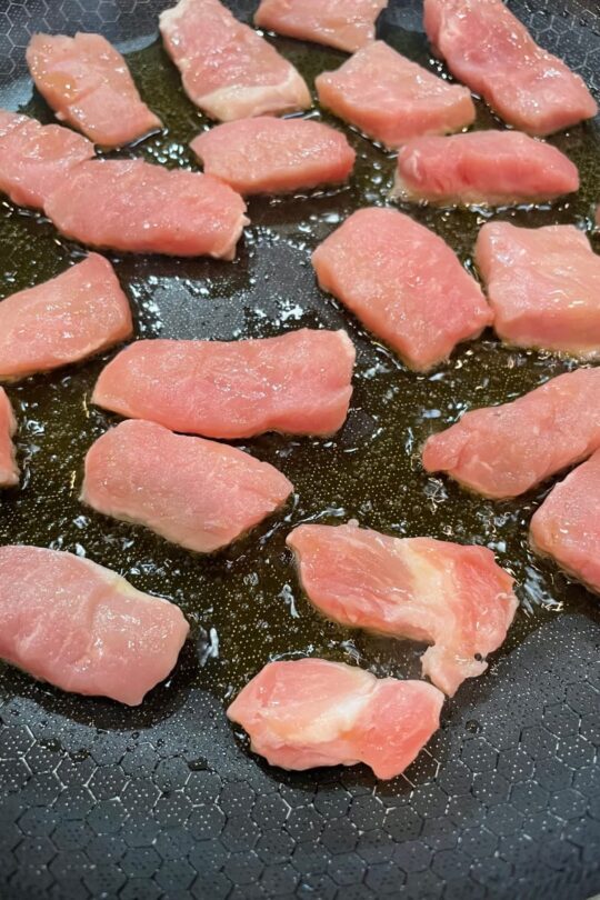 Frying chicken breast in a skillet for ginger noodles with chicken. 