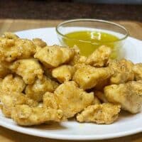 Boneless lemon pepper chicken wings on white plate with dipping sauce.