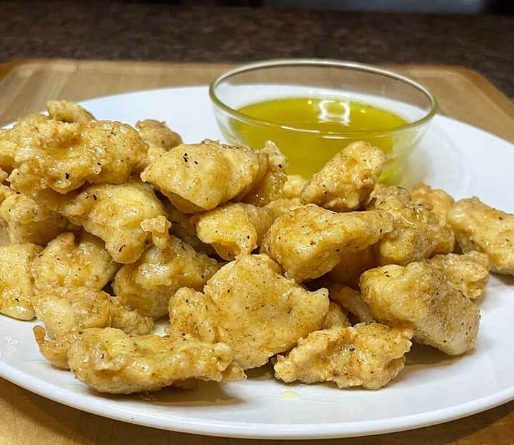 Boneless lemon pepper chicken wings on white plate with dipping sauce.