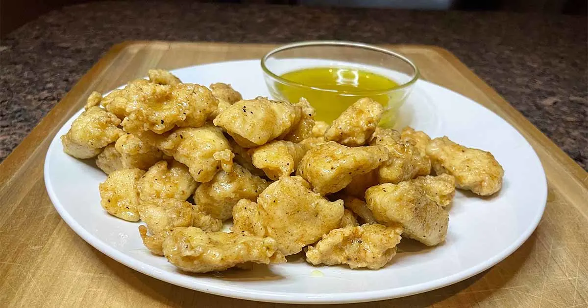 Boneless lemon pepper chicken wings on white plate with dipping sauce.