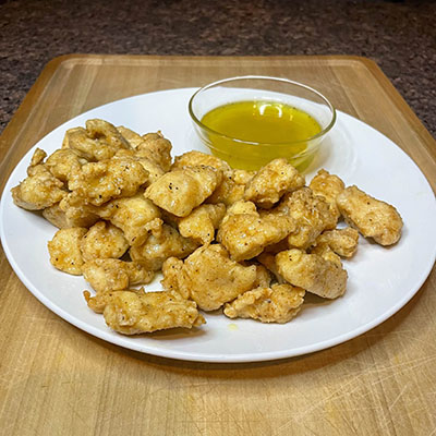 Boneless lemon pepper chicken wings on white plate with dipping sauce.