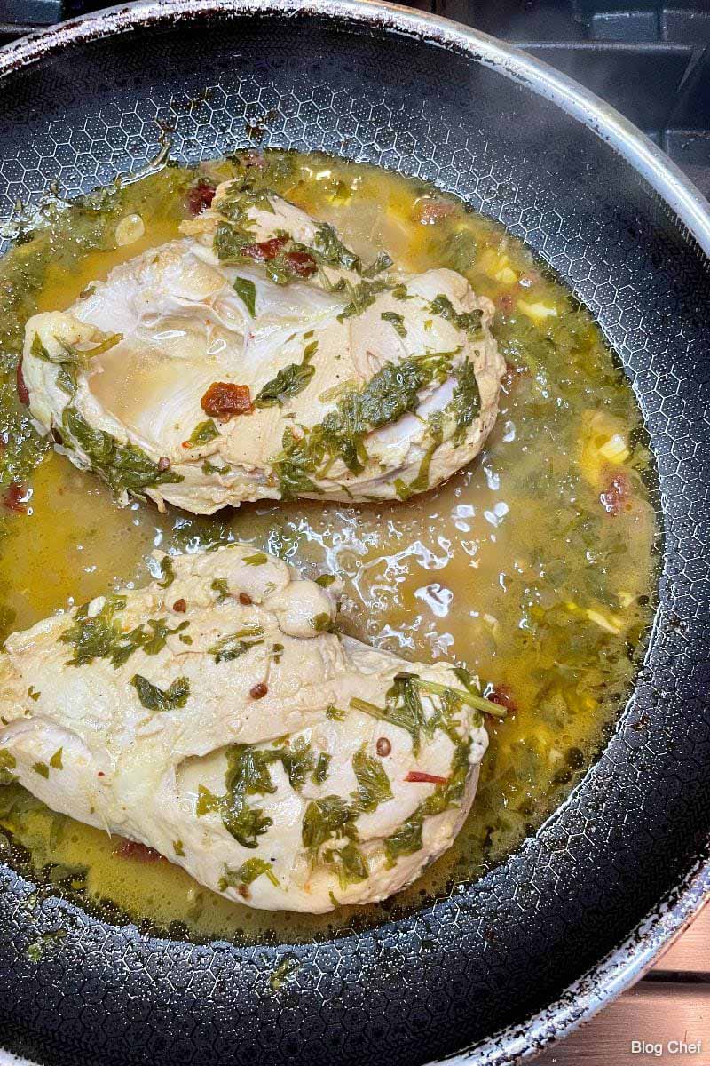 Two chicken breasts cooking in cilantro citrus sauce in a large skillet.