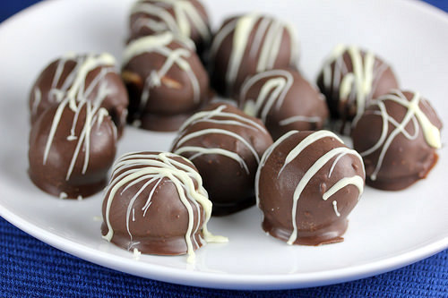 Peanut butter balls coated in chocolate with white drizzle on serving plate