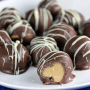 Peanut butter balls coated in chocolate with white drizzle on serving plate