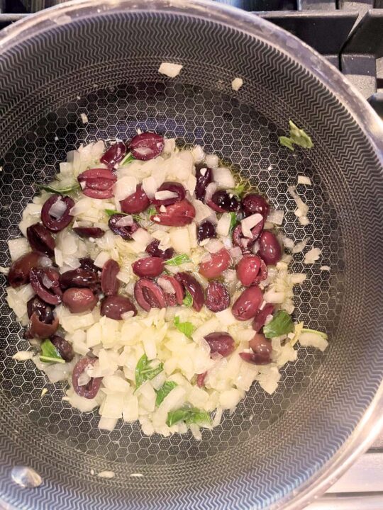 Chopped onions, basil, and kalamata olives in skillet.