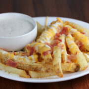 Aussie cheese fries with melted cheese and bacon pieces beside a bowl of dip