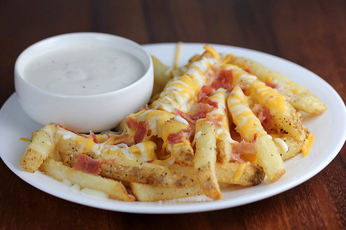 Aussie cheese fries with melted cheese and bacon pieces beside a bowl of dip