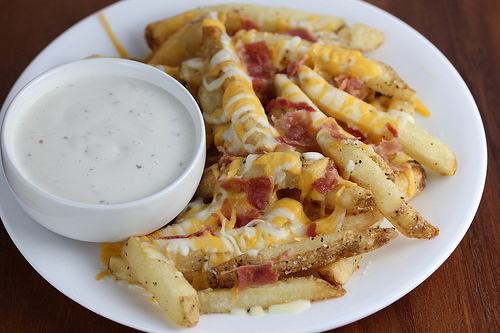 Aussie cheese fries with melted cheese and bacon pieces beside a bowl of dip