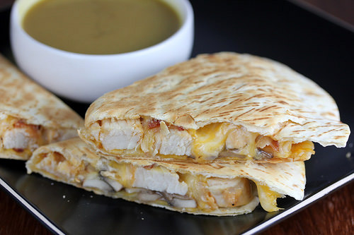 Quesadilla slices filled with chicken, cheese, and bacon on a black plate with dipping sauce