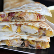 Quesadilla slices filled with chicken, cheese, and bacon on a black plate with dipping sauce