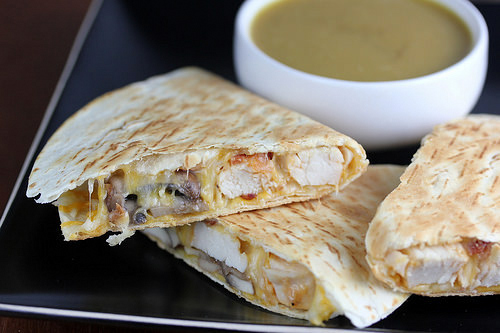 Quesadilla slices filled with chicken, cheese, and bacon on a black plate with dipping sauce