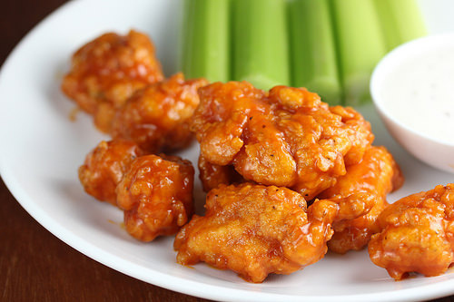 Spicy chicken bites served with celery and dipping sauce on a white plate