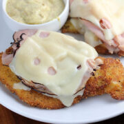 Malibu chicken with ham and melted cheese served with dipping sauce on a white plate.
