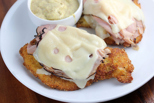 Malibu chicken with ham and melted cheese served with dipping sauce on a white plate.