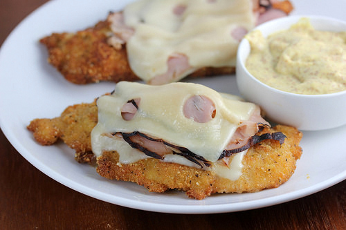 Malibu chicken with ham and melted cheese served with dipping sauce on a white plate.