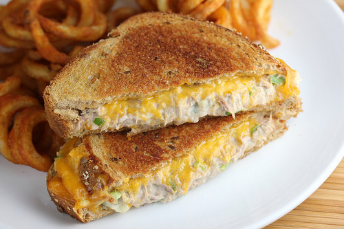 Grilled tuna and cheddar sandwich served with curly fries on a white plate