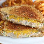 Grilled tuna and cheddar sandwich served with curly fries on a white plate