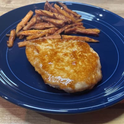 Prepared baked pork chop on plate with sweet potato fries.