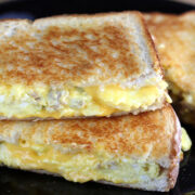 Egg and sausage grilled cheese sandwiches sliced and stacked on a black plate.